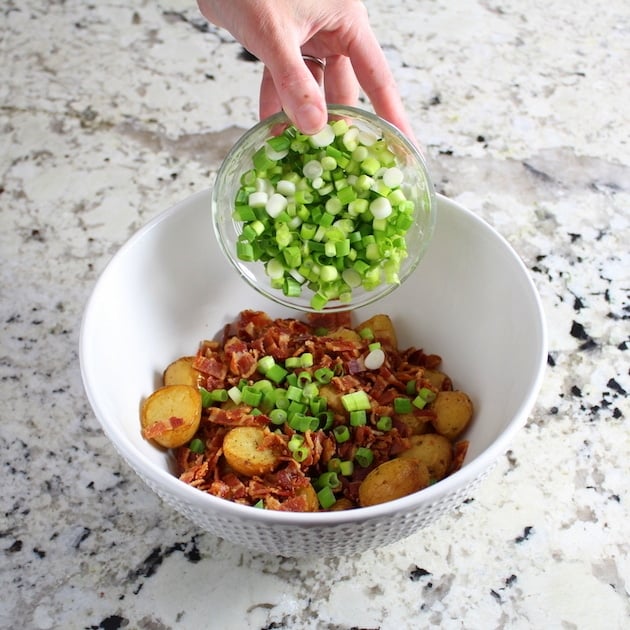 Adding chopped green onions to mixing bowl with bacon and potatoes