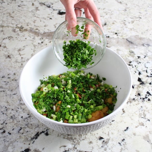 Adding chopped parsley to mixing bowl of potato salad