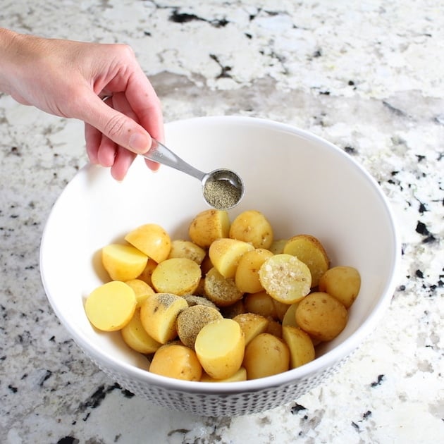 Adding pepper to bowl of cut up baby potatoes