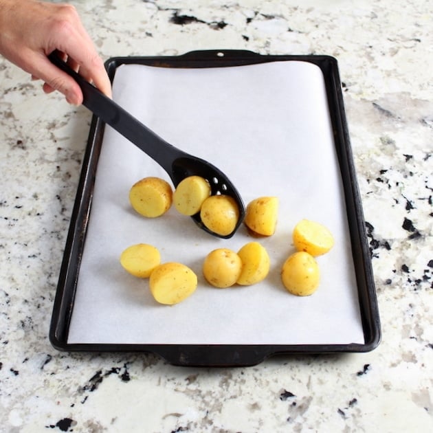 Adding potatoes to baking sheet with parchment paper