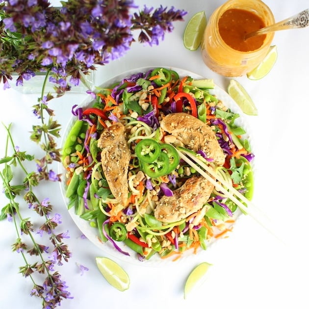 Asian salad with Chicken Satay on table with purple flowers, and mason jar of peanut dressing