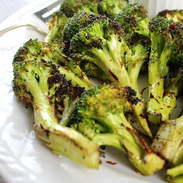 Grilled Broccoli florets stacked on white plate