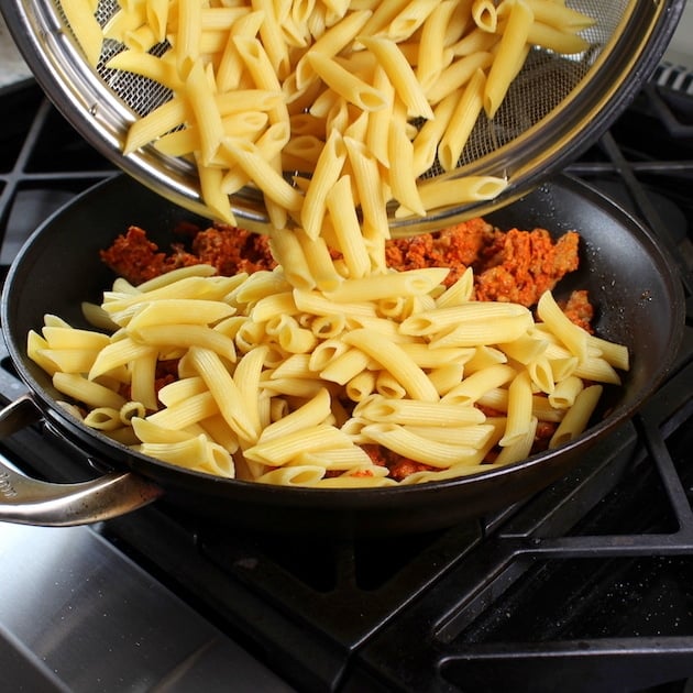 Adding penne pasta to Spicy Chicken Pasta on stovetop