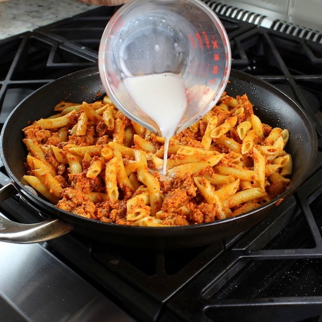 Adding almond milk to Spicy Chicken Pasta on stovetop