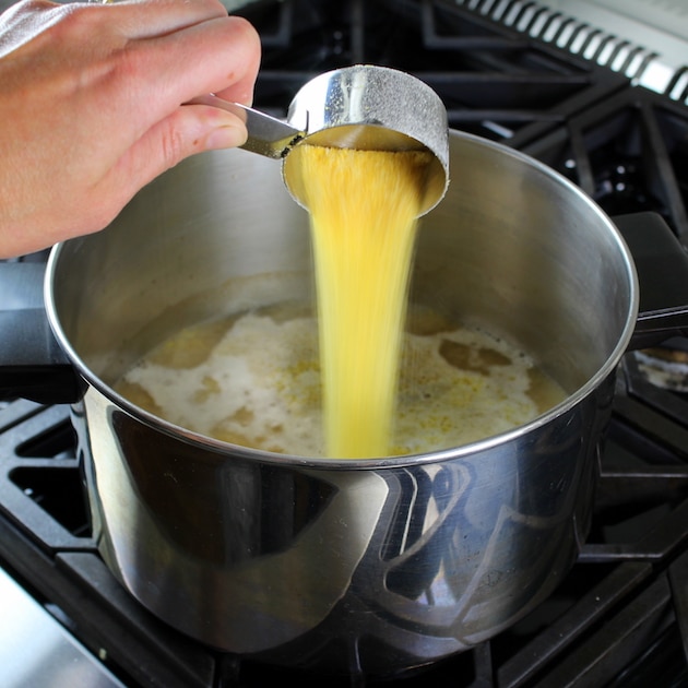 adding polenta to a pot with chicken stock