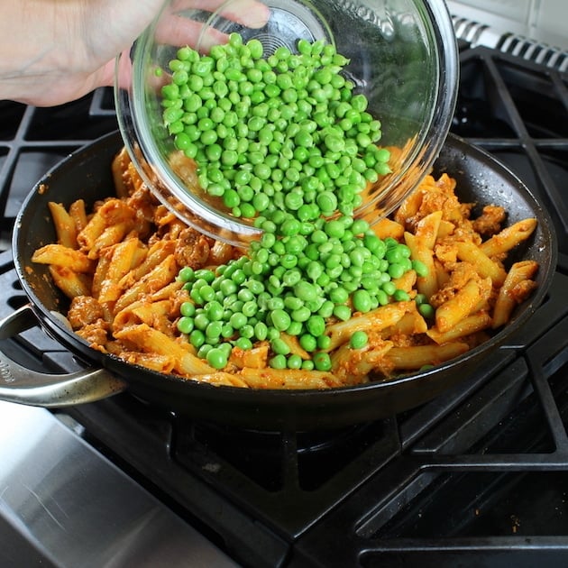 Adding peas to Spicy Chicken Pasta and Peas with Sun-Dried Tomato Sauce on stove top