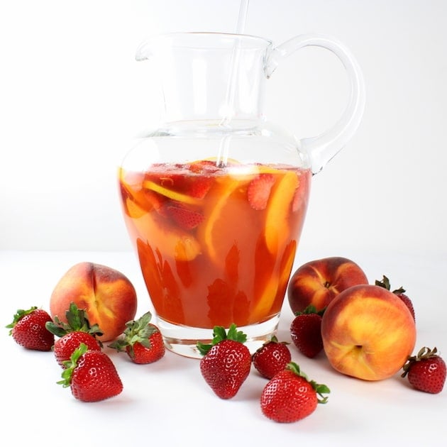Sliced of fresh fruit and vegetables in a large glass pitcher with peach sangria