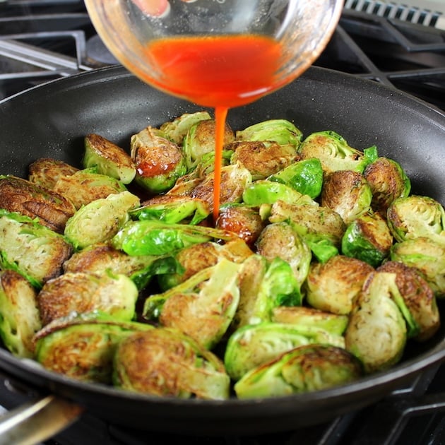 Pouring honey sriracha sauce into a saute pan full of Brussels Sprouts