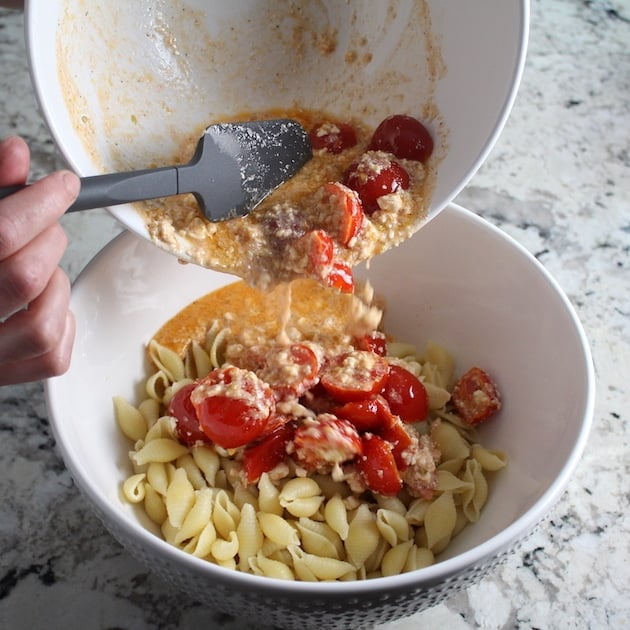 Pouring tomato feta sauce into bowl of cooked pasta