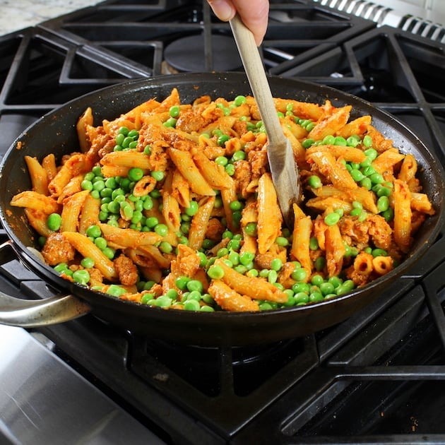 Wooden spoon stirring Spicy Chicken Pasta and Peas with Sun-Dried Tomato Sauce