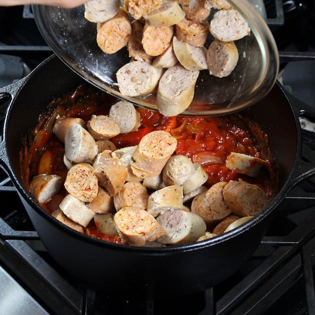 Adding cooked sausage to pot with red sauce