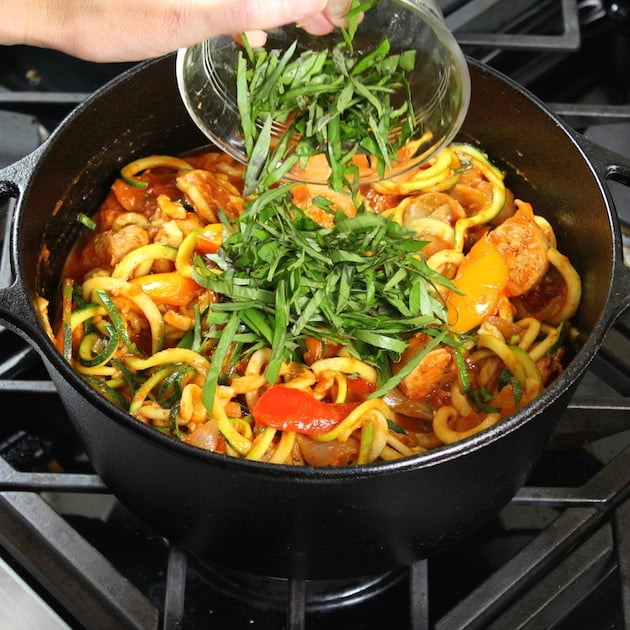 Adding herbs to pot of italian sausage with peppers and zoodles