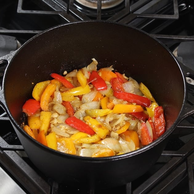 peppers and onions cooking in a large black cast iron pot