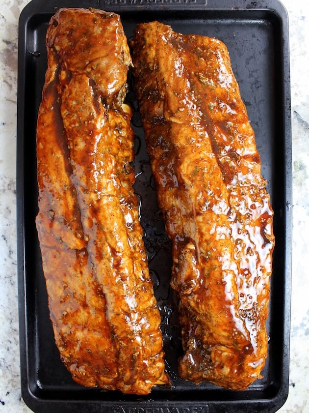Two racks of ribs covered in BBQ sauce before grilling