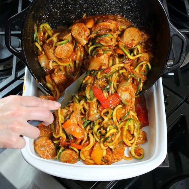 Filling a casserole dish with italian sausage, peppers, zoodles, and red sauce