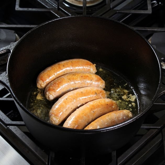 Italian sausages cooking in a large black cast iron pot