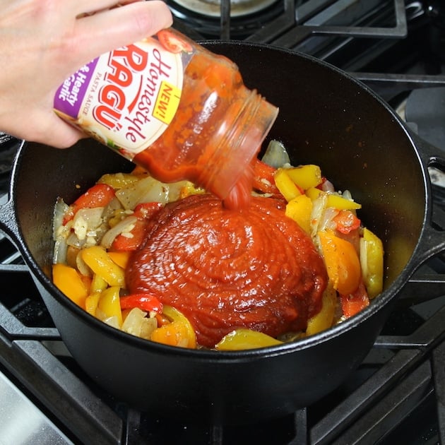 adding red marinara sauce to pot with peppers and onions