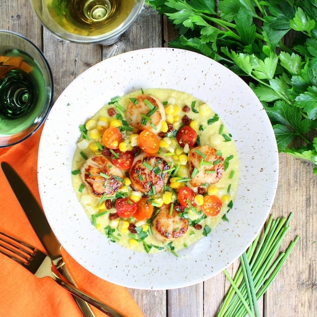 Bowl of Pan-Seared Sea Scallops over Corn Puree with greens and glass of wine