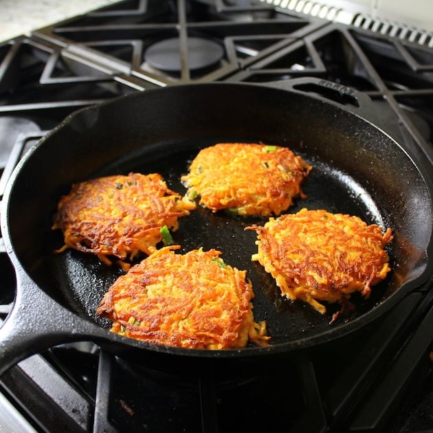 Four Sweet potato cakes frying in a cast iron skillet