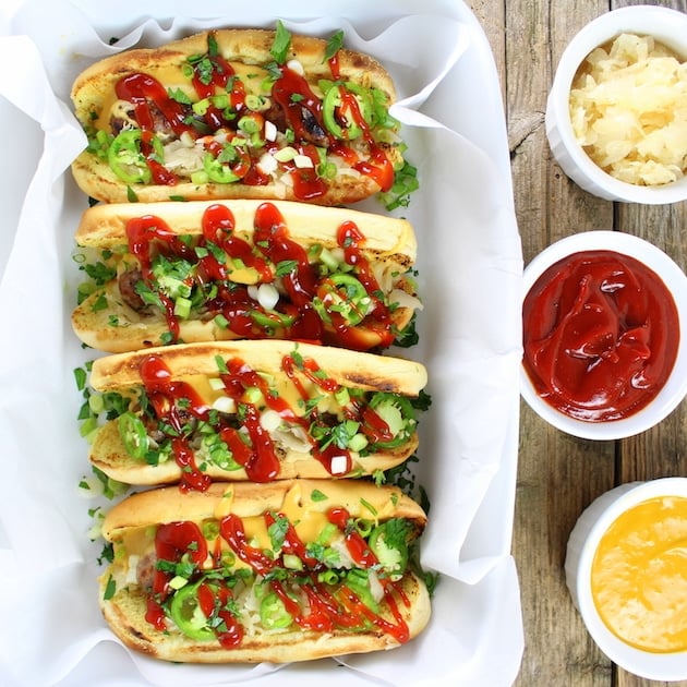 4 Cheesy Beer Brats in a row with ramekins of condiments