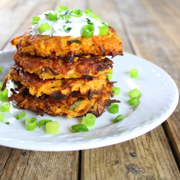 Sweet potato cakes stacked on a plate and topped with sour cream & green onions