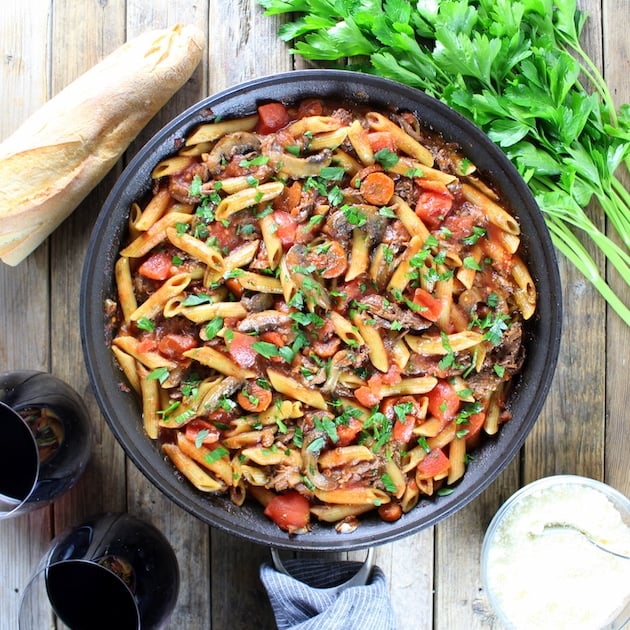 Crock-Pot Beef Ragu with Penne and Ricotta in saute pan with parsley, wine, and baguette