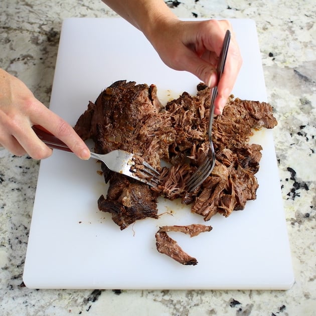 Using two forks to pull slow-cooked Beef on a cutting board 