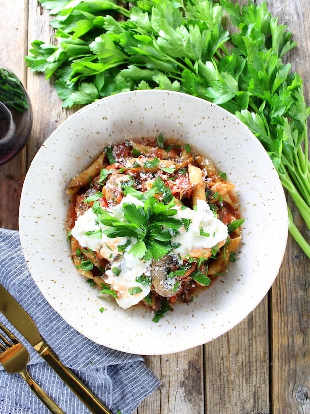 Bowl of slow cooker Beef Ragu with Penne and Ricotta, on farm table with silverware