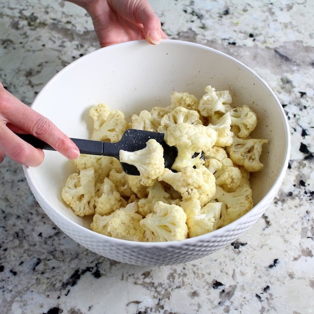 Stirring cauliflower florets into a mixture of olive oil