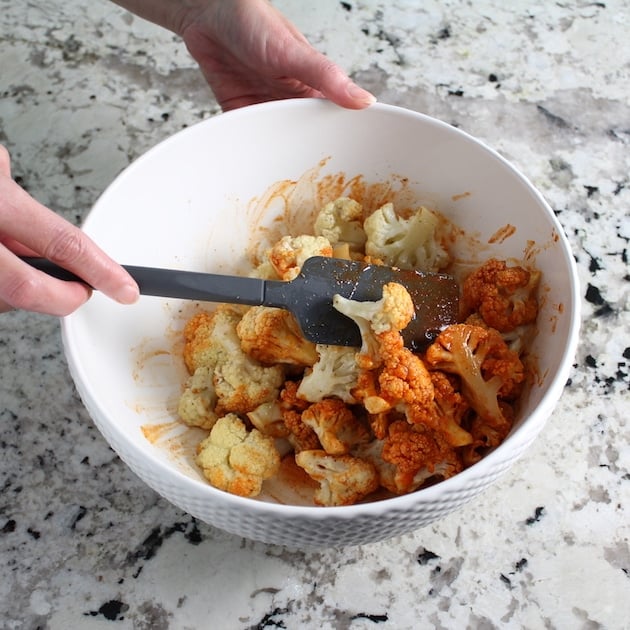 Stirring red hot buffalo sauce into roasted cauliflower florets 