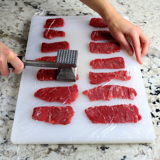 pounding beef under saran wrap on cutting board