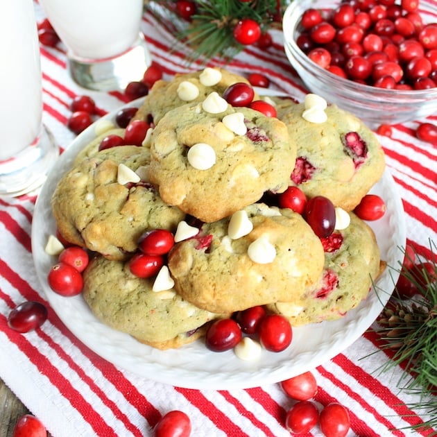 A plate stacked with Cranberry Orange Cookies with a glass of milk on a holiday table cloth.