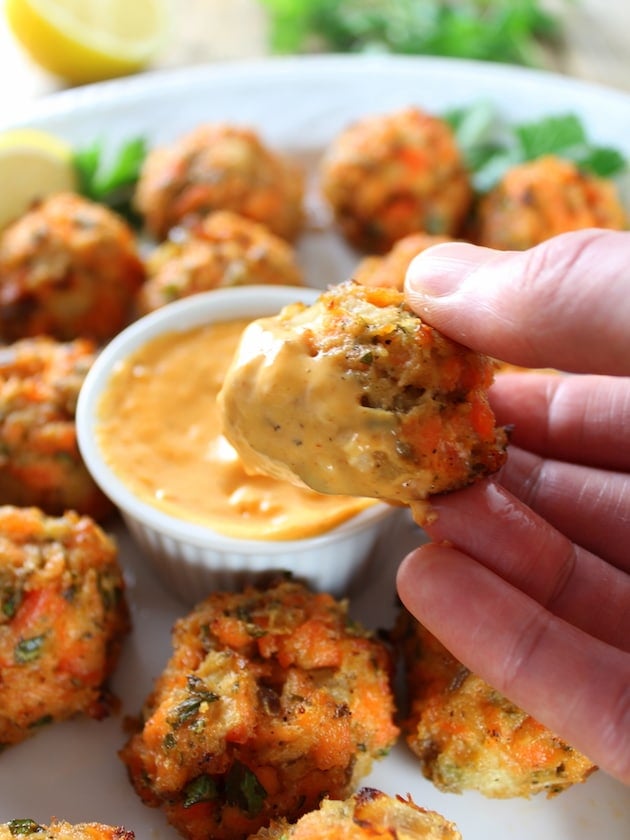 A person holding a Salmon Cake dipped in Sriracha Lemon Aioli.