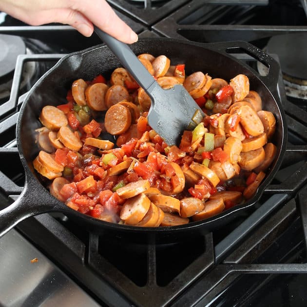 Stirring sliced chicken sausage into skillet of veggies