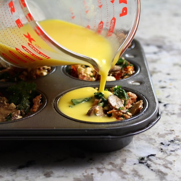 Pouring egg over ingredients in muffin tin to make breakfast cups