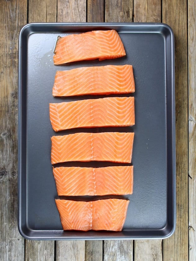 Side of salmon sliced into pieces on a baking sheet ready to cook