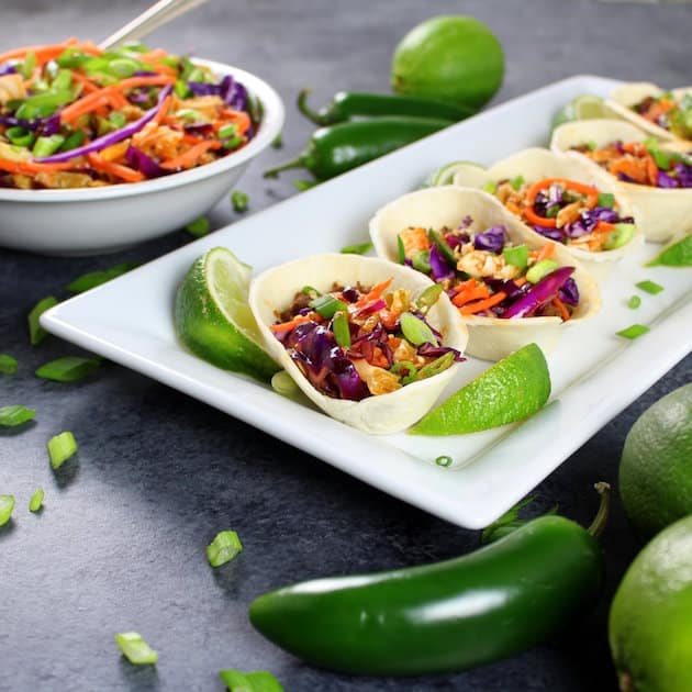 Eye level platter of Mini Taco Boats with bowl of Spicy Asian Slaw