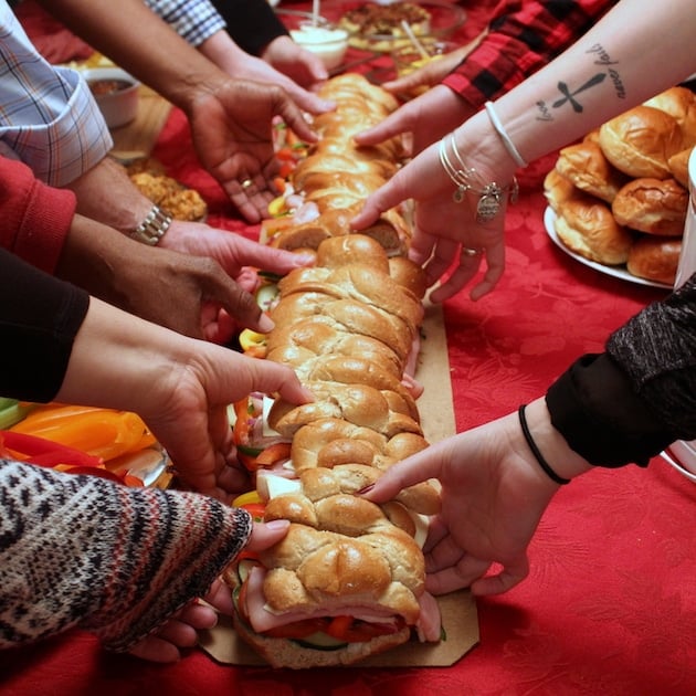 A lot of different hands reaching in for a piece of a giant sub sandwich