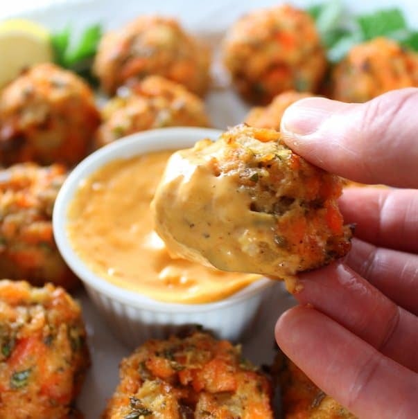 Close up hand holding a Mini Salmon Cake dipped in Sriracha Lemon Aioli