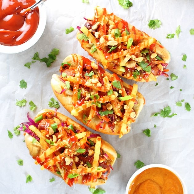 Three Asian hot Dogs with french fries, Asian slaw, and Sriracha Ketchup on parchment paper