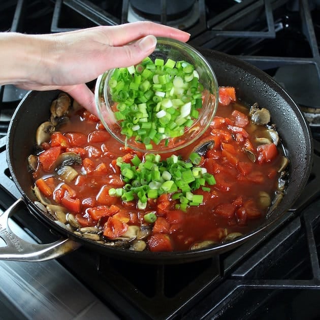 Adding green onions to saute pan with tomatoes and mushrooms