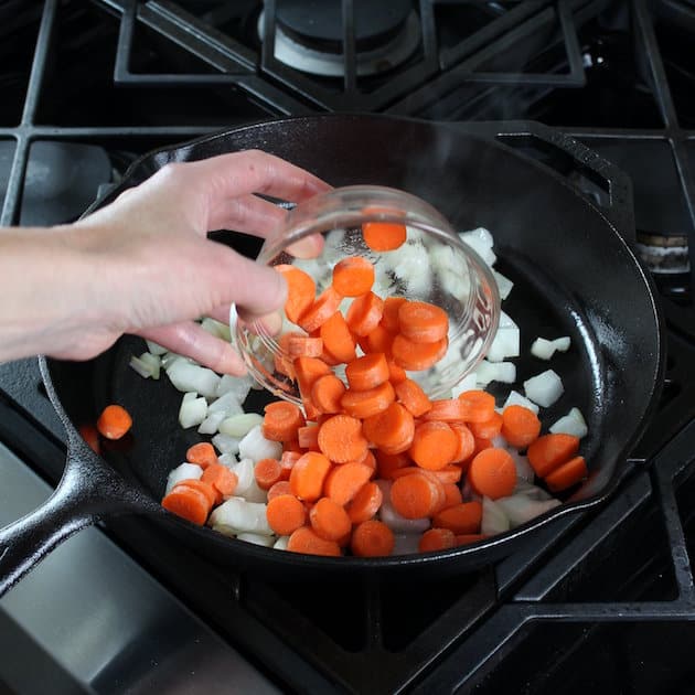 Adding carrots to onions in skillet on stovetop