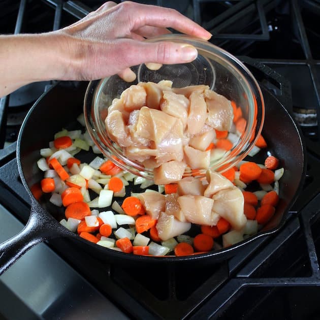 Adding chicken to skillet with onions and carrots