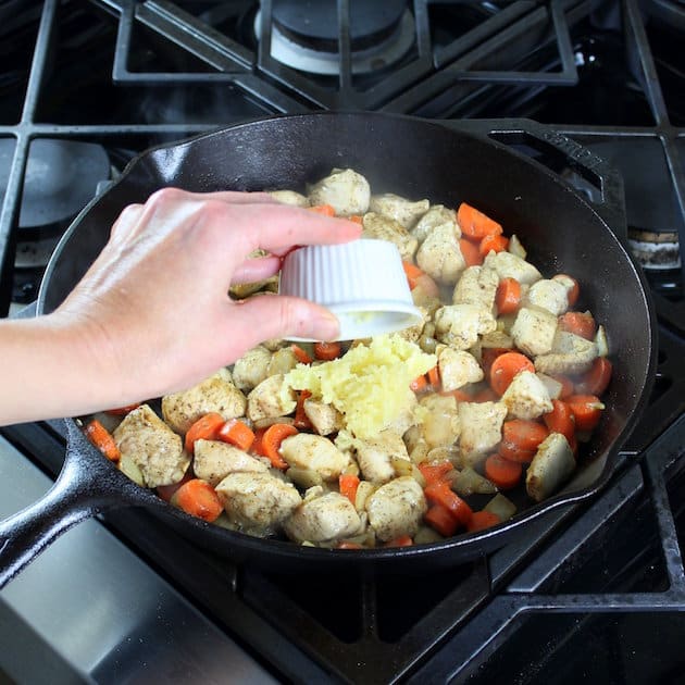 Adding garlic to a pan filled with meat and vegetables 