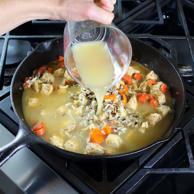 adding chicken stock to skillet of sweet potatoes and wild rice