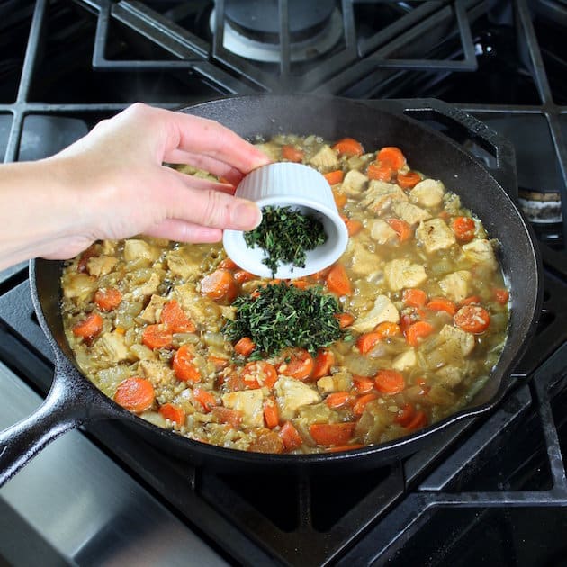 Adding thyme to skillet of cooking vegetables and chicken