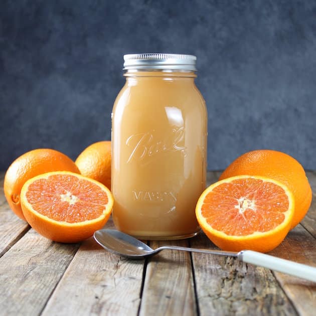Two oranges cut in half and a mason jar of orange-vinegar drink