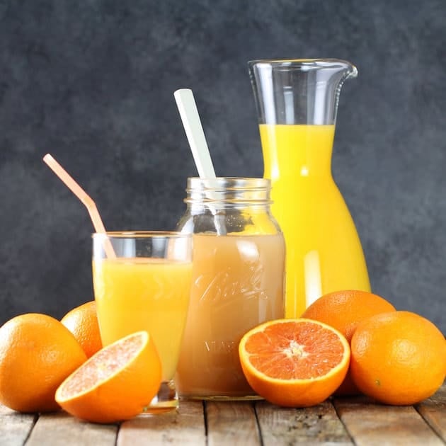 Halved oranges and glass of OJ on farm table with pitcher in background