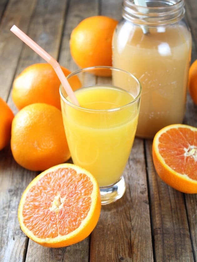 Two oranges and a glass of orange juice