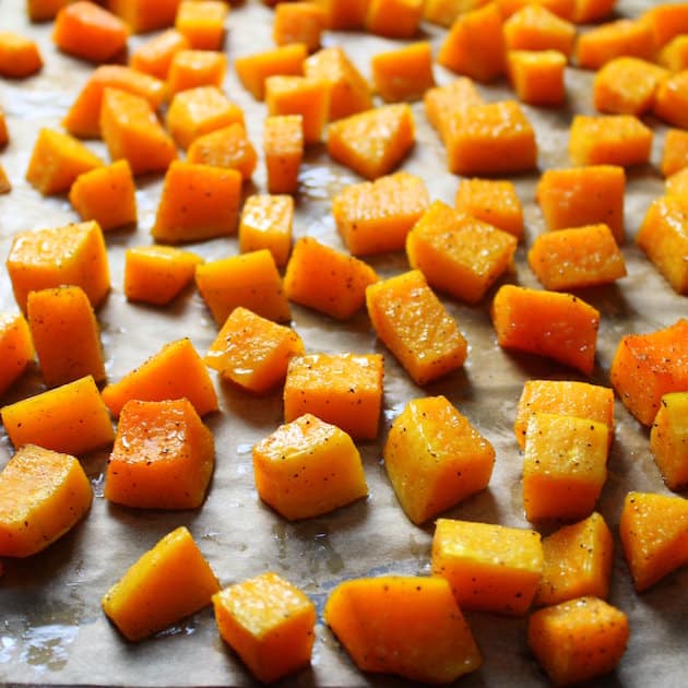cubed butternut squash roasting on baking sheet with parchment paper 